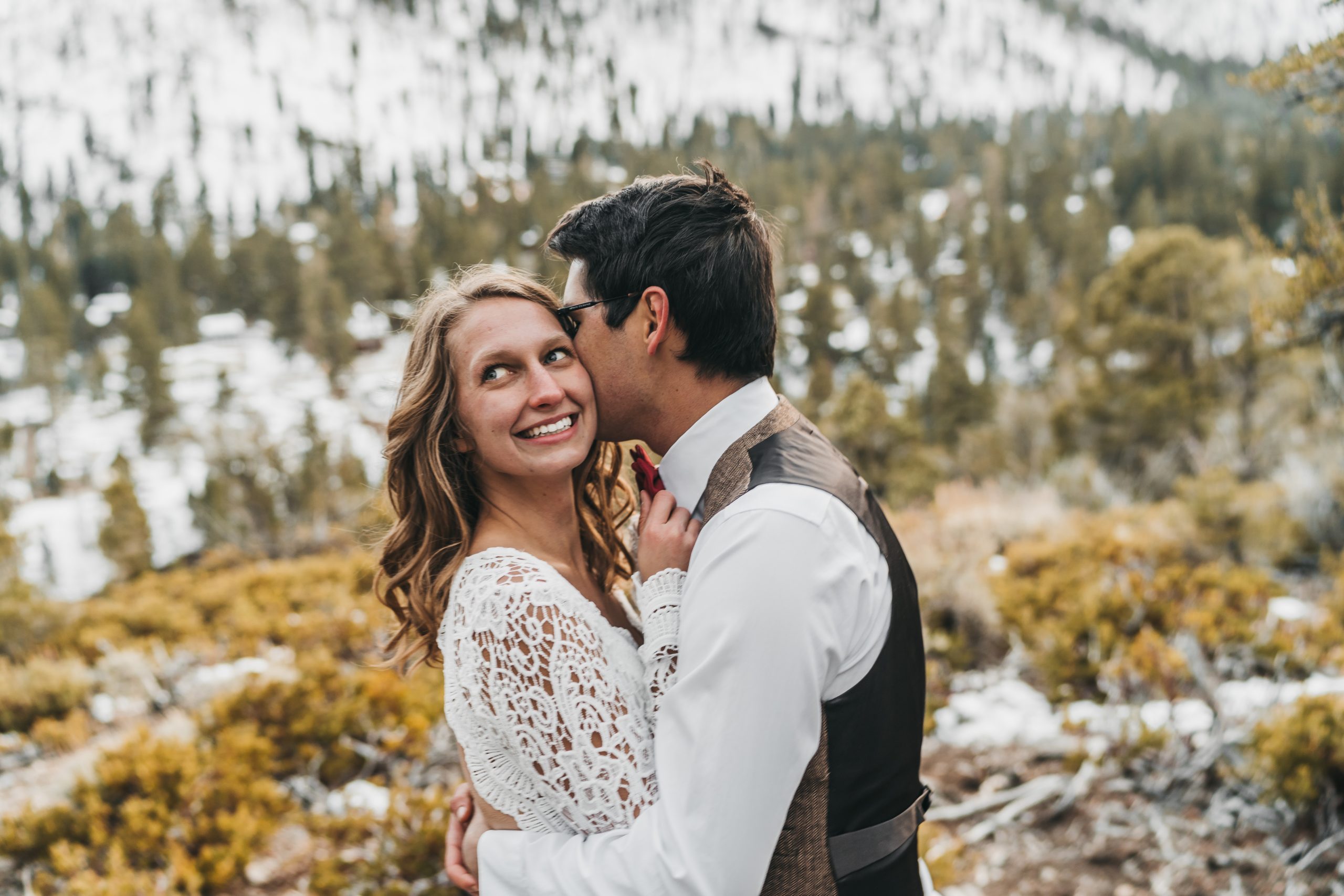 Couple in the mountains snuggled up close wearing wedding clothing.
